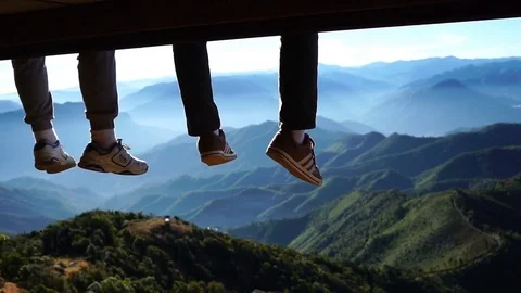 Two men legs hanging from the bench against a blue sky and mountains view. Video stock 71570061