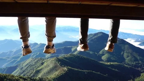 Two men legs hanging from the bench against a blue sky and mountains view. Stock Footage 71570257