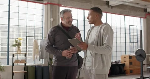 Two men in loft studio, right man holding tablet initiating workout plan review, Stock Footage 337255228