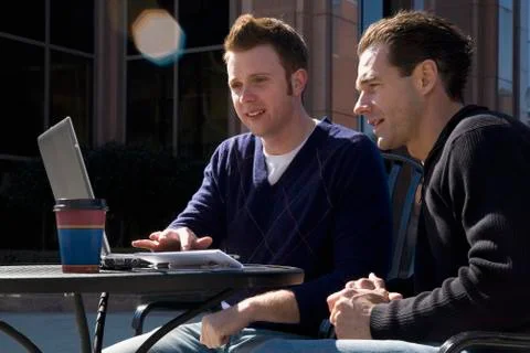 Two men looking at a laptop computer at an outdoor cafe Stock Photos