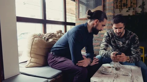 Two men looking at mobile phone and talking seriously in a cafe Stock Footage 95902539