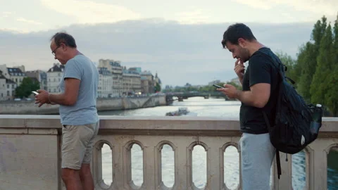 Two men looking on a smartphone for a map on a bridge in Paris Stock Footage 231196662