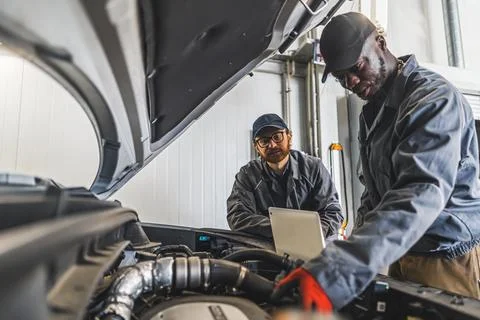 Two men mechanics completing car engine diagnostics with laptop in a repair shop Stock Photos