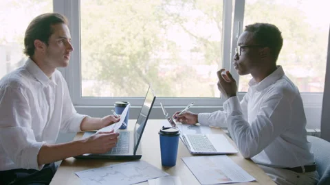 Two men meet in an office space discuss business matters while using laptops 스톡 동영상 335731667