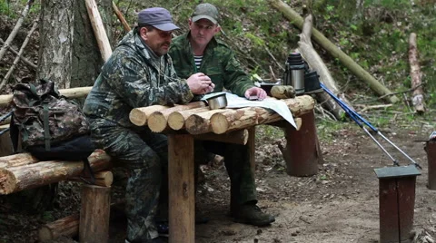 Two men in military uniform sitting at a table of logs in a transit camp in the Stock Footage