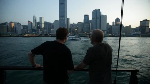 Two men on moving boat in Harbor admire the view of Hong Kong cityscape at dusk Video stock 89301125