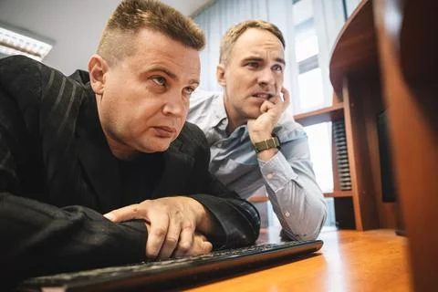 Two men in office intensely thinking over report while looking at computer .. Stock Photos