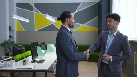 Two men in the office in suits are talking, smiling, shaking hands, negotiating. Stock Footage 233993772