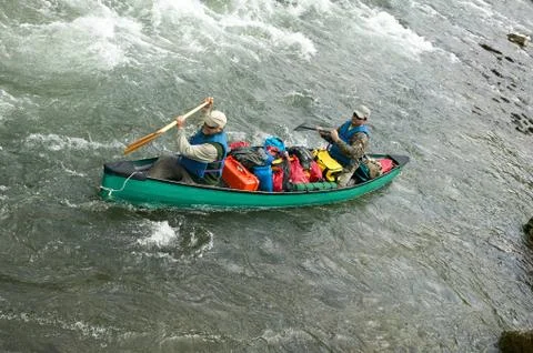 Two men in packed canoe on wild river rapids Stock Photos