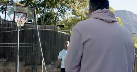 Two men passing basketball at backyard hoop, man in light pink hoodie receiving Vídeo Stock 342085266