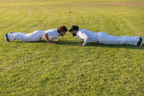 Two men performing push-ups on grass field in white uniforms with orange Stock Photos