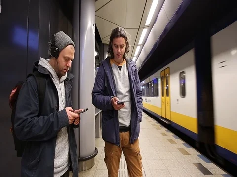 Two men with a phone stand on the platform with fast passing train Stock Footage 83223772