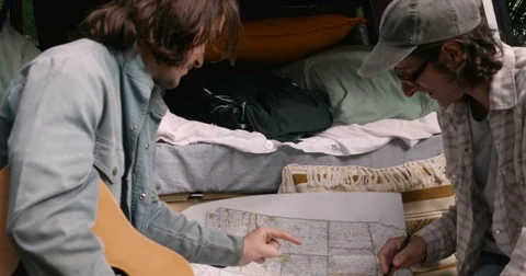 Two men planning their road trip in the USA looking and pointing at a paper map Stock Footage 80809351