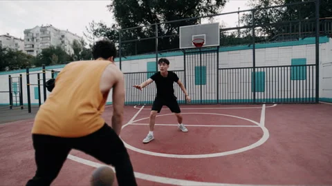 Two men play intense streetball on an outdoor court with dribbling and defense 库存影片 344679339