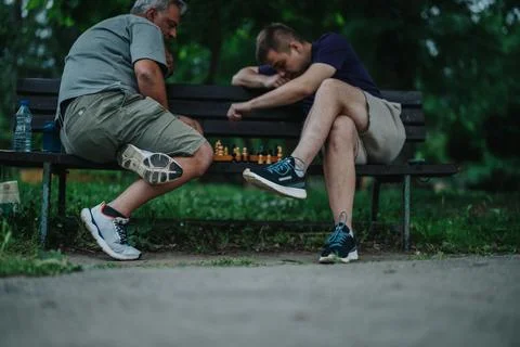 Two men playing a chess game on park bench in casual setting Stock Photos