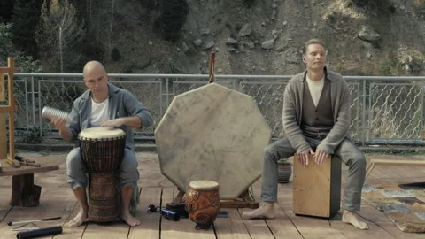 Two men playing ethnic percussion instruments outdoors. natural mountain setting Vidéo 300889924