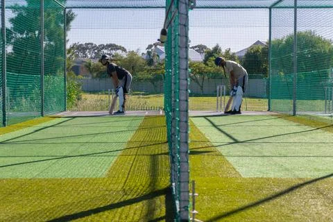 Two men practicing batting in adjacent cricket nets with wooden bats, helmets, Stock Photos