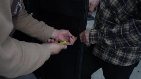 Two men putting a screw to a plastic door with a yellow screwdriver Stock Footage 140753137