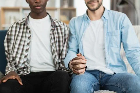 Two men in relations holding hands while sitting on sofa 库存照片