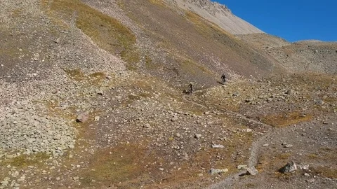 Two men ride along the mountain path full of rocks. Video stock 83763619