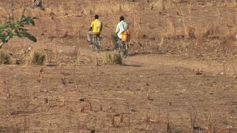 Two men ride bicycles along a dusty path through the dry northern Ghana savanna Video stock 321923341