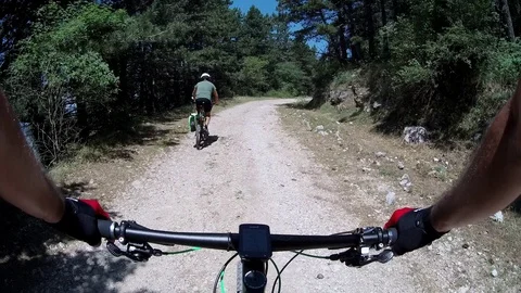 Two men ride bycicles fast down on a forest path, sunny summer morning POV Stock Footage 113284807