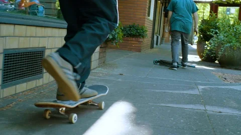 Two men riding push scooter and skateboard on the pavement Stock Footage 87804822
