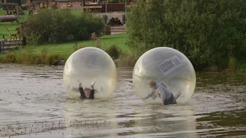 Two men run into each other while running in a zorbing ball on the water Stock Footage 248846746