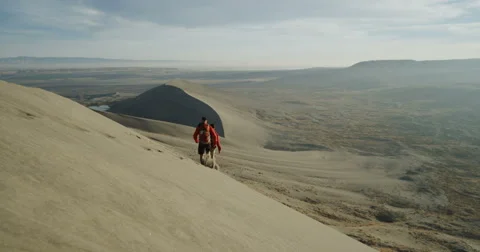 Two men running down a sand dune in the desert in slow motion Stock Footage 64332625