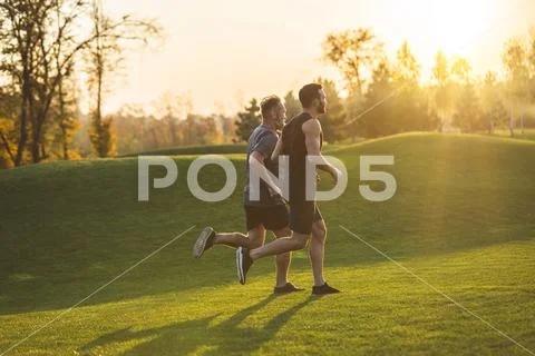 The two men running on the grass in the park on the sunrise background Stock Photos
