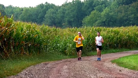Two Men Running Together Down Dirt Field Lane with Scenic Corn Field Stock-Footage 71325252