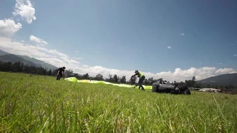 Two men saving the parachute after a paraglide in a green grass field with 스톡 동영상 133379692