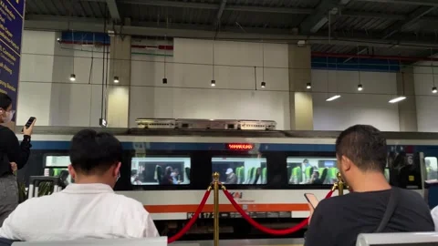 Two men seated and waiting as a commuter train passes by on the platform. Видео 334377204