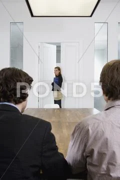 Two men seated at a table and a woman entering a conference room Stock Photos