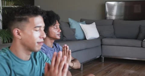 Two men settling onto living room floor, sitting cross-legged, pressing palms Stock Footage 340774065