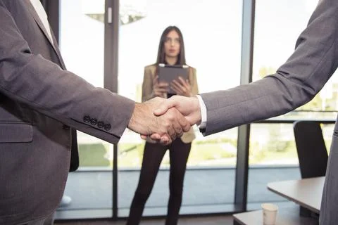 Two men shake hands in front of a woman Фото