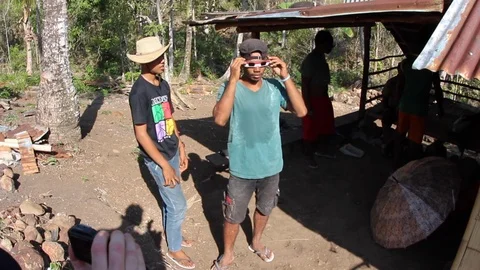 Two men share eclipse viewing glasses to look at the sun in Indonesia. Stock Footage 114716903