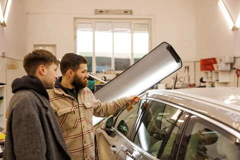 Two men sharing a conversation while gesturing at a car in a garage who have Stock Photos