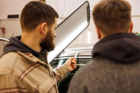 Two men sharing a conversation while gesturing at a car in a garage Stock Photos