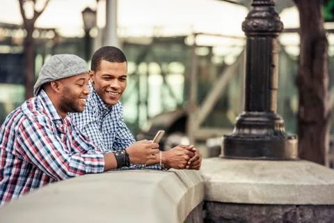 Two men side by side leaning on a parapet by a bridge looking at a smart phone Stock Photos
