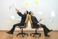 The two men sit on chairs and throwing papers on the white wall background Photo