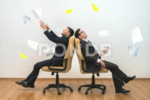 The two men sit on chairs and throwing papers on the white wall background Stock Photos