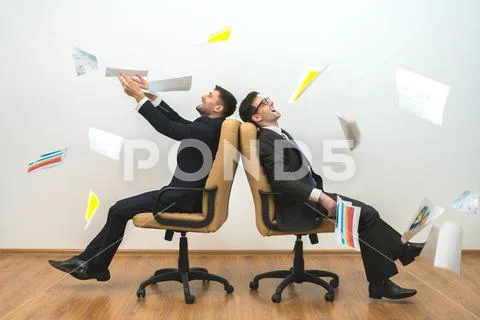 The two men sit on chairs and throwing papers on the white wall background Stock Photos