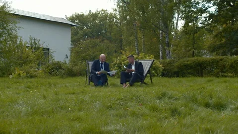 Two men sit in chairs with papers and talk. Stock Footage 118378752