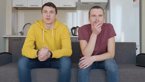 Two men sit on the couch and in anticipation of watching a football match on TV Stock Footage 107648367