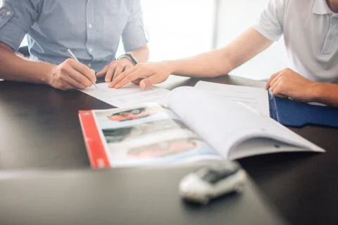 Two men sit at table. Guy on left signing papers while man on left points wit Stockfoto's