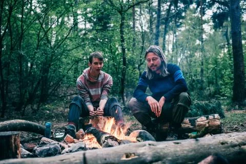 Two men sitting around campfire in spring forest. Stock Photos