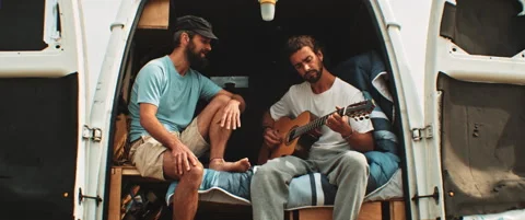 Two men sitting in back of a van singing and playing the guitar Stock Footage 203584513
