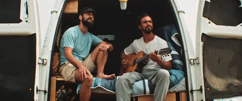Two men sitting in back of a van singing and playing the guitar Stock Footage 203584521
