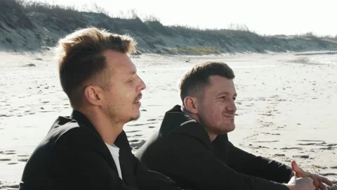 Two men sitting on the beach talking. They drink alcohol. Video stock 155489733